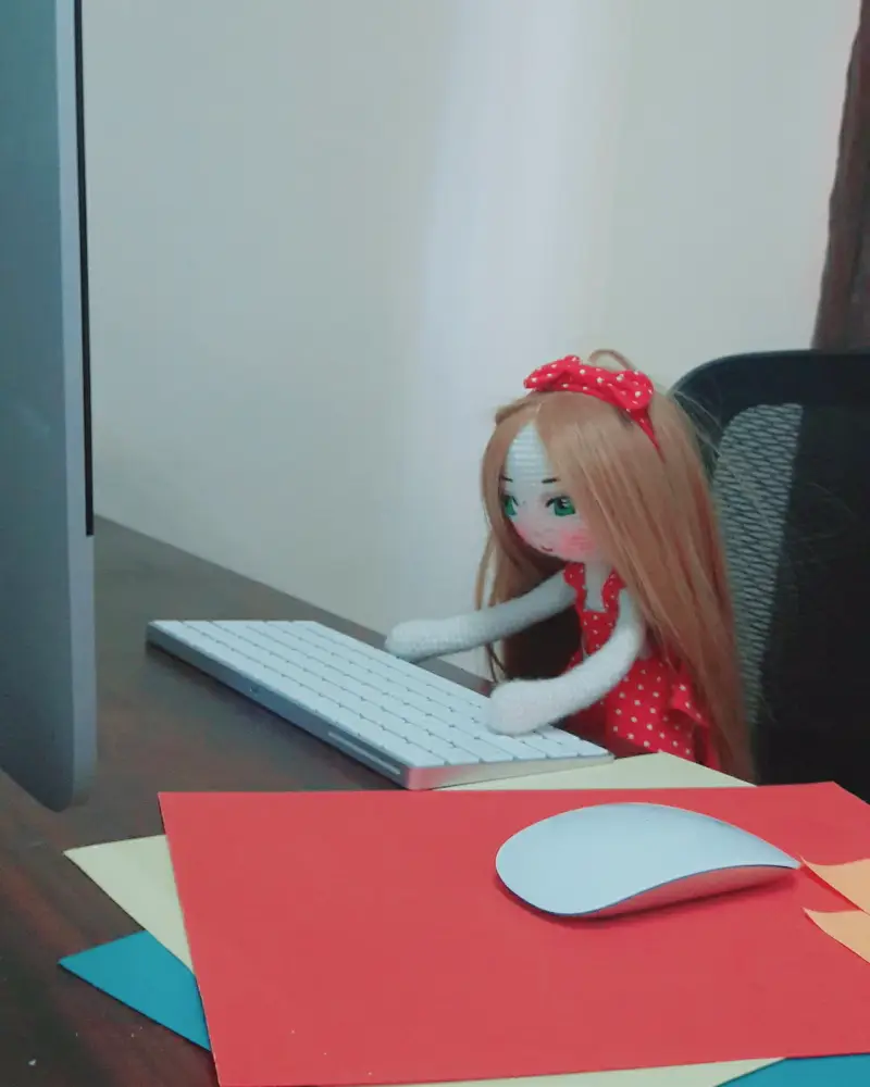 A handmade doll sitting at a desk with its hands on a keyboard, in our office